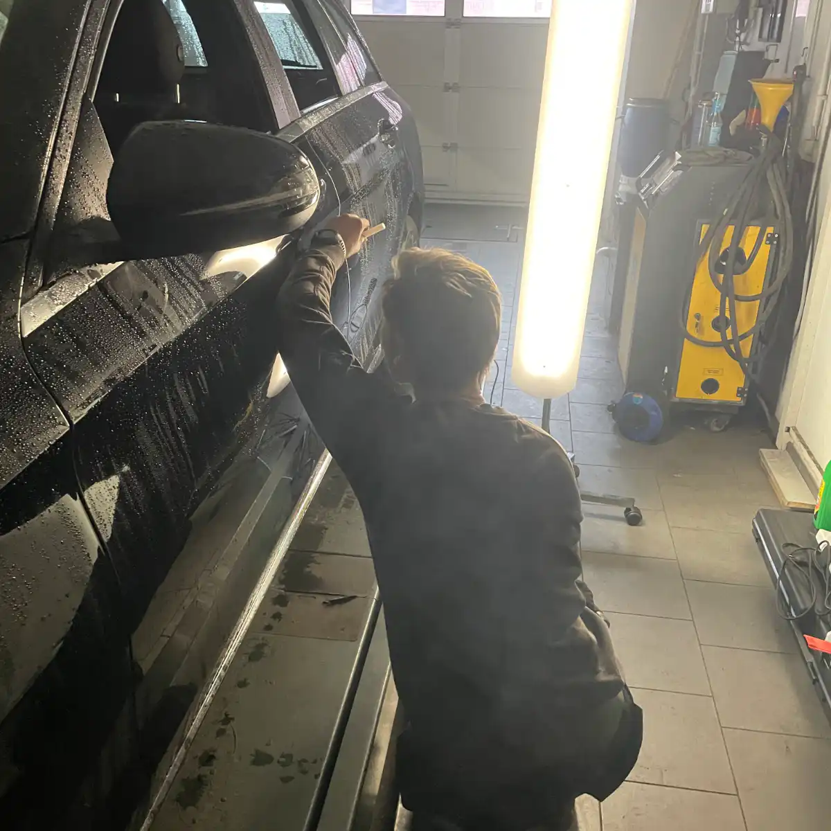 Person poliert Auto in Werkstatt.