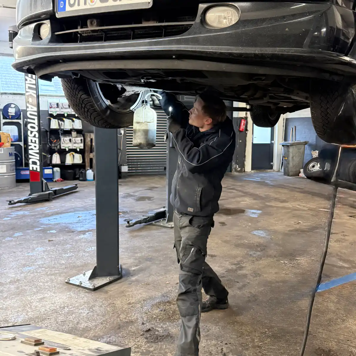 Mechaniker arbeitet unter angehobenem Auto in Werkstatt.